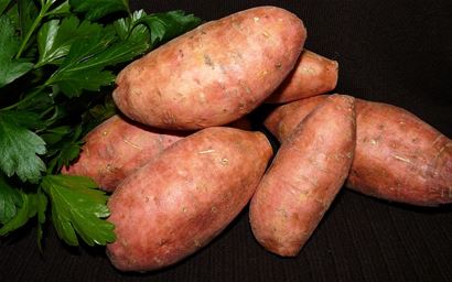 several sweet potatoes on a dark background with leaves