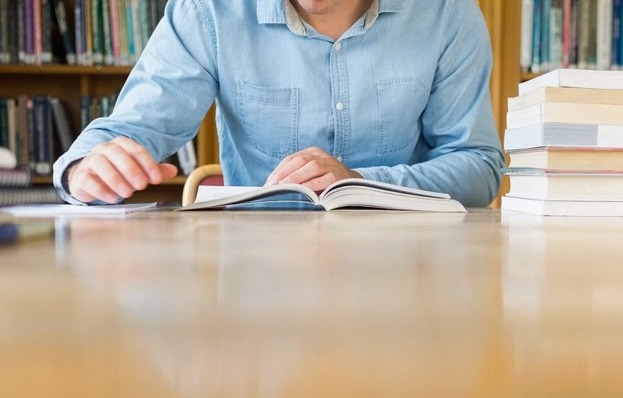 Mid section of a mature male student studying at desk in the library